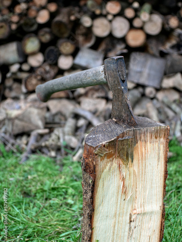 An axe stuck in a firewood log. Lot of firewood logs in blurred background.