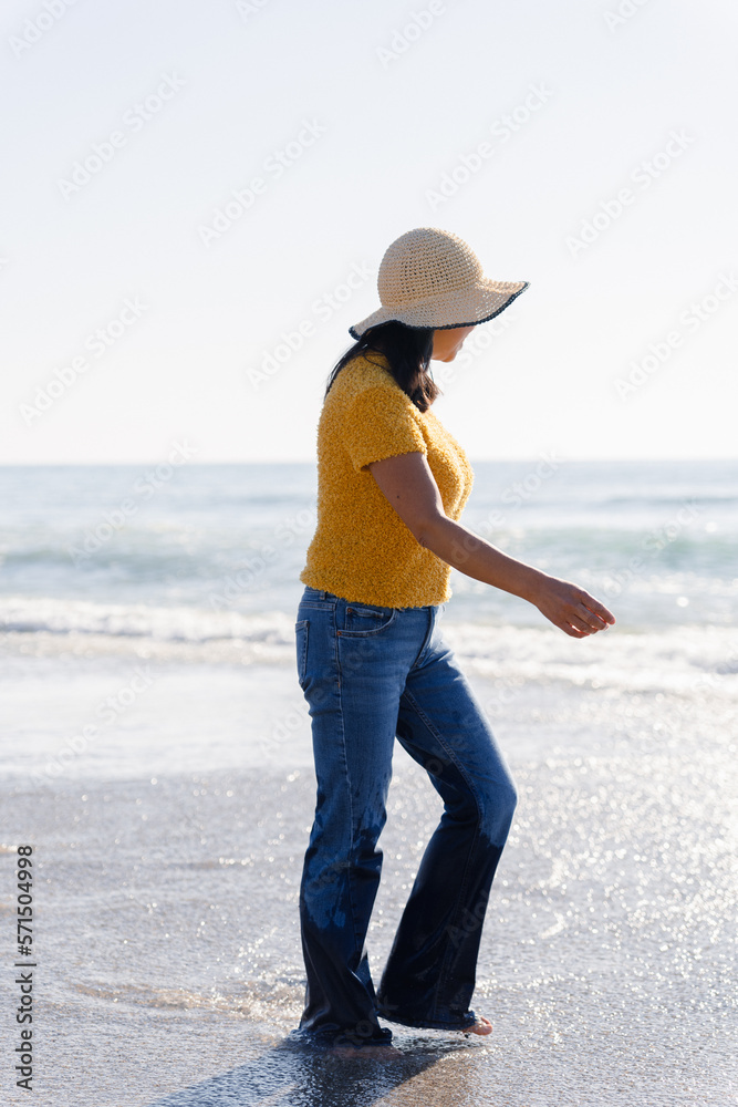 Unknown Latin woman with hat running on the shore of the beach in a splendid spring day. 