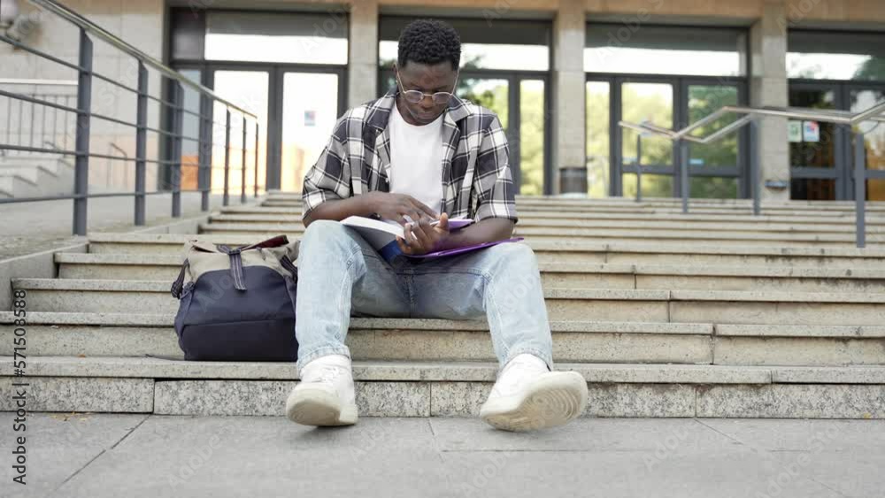 African Male Student studying reading book sitting on University College staircase African Male Student studying reading book sitting on University College staircase