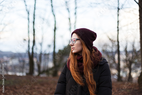 red-haired woman in a hat and down jacket in the middle of the park