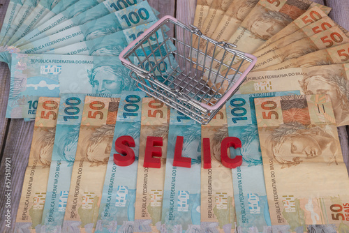 Notes of 50 and 100 reais on wood with a mini supermarket basket, with the word SELIC which means in Portuguese 