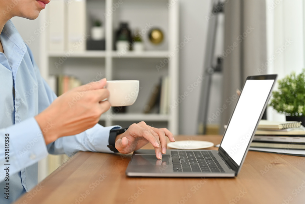 Cropped image of businessman hand holding cup of coffee and using laptop computer at working desk