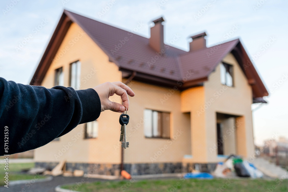 Key in a hand in front of home. Building, project, moving to new home, mortgage, rent and purchase real estate. Key in a hand in front of home. Building, project, moving to new home, mortgage, rent and purchase real estate.