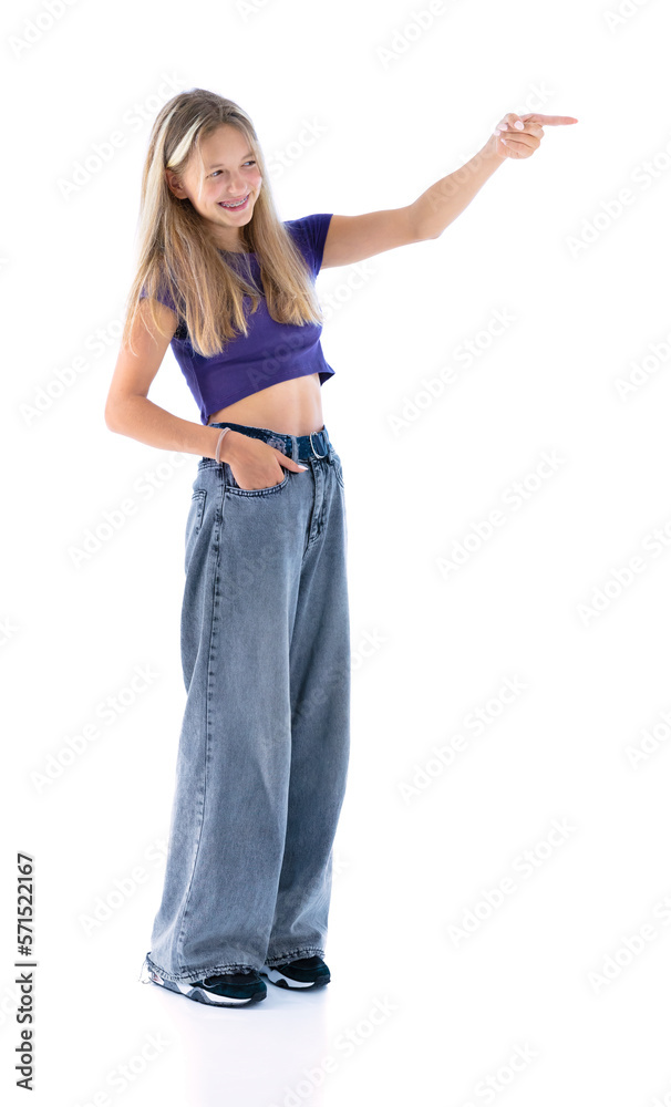 Full length portrait of cute girl in violet T-shirt and blue jeans pointing at side and smiling isolated on white background. Beautiful female teenager posing in studio. Full length portrait of cute girl in violet T-shirt and blue jeans pointing at side and smiling isolated on white background. Beautiful female teenager posing in studio.