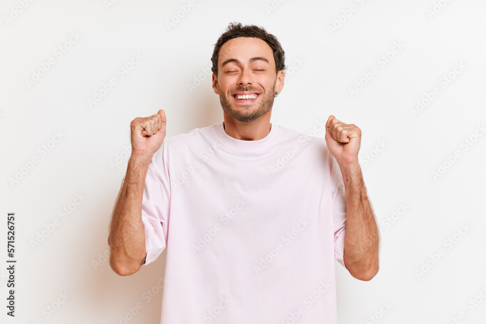 Young caucasian man wearing white casual t-shirt smiles excited and happy with arms raised and eyes closed celebrating victory isolated over white background. Winner concept. Young caucasian man wearing white casual t-shirt smiles excited and happy with arms raised and eyes closed celebrating victory isolated over white background. Winner concept.