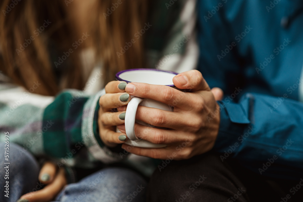 Hands of millennial caucasian woman and guy in jackets hold cup of hot drink, travel in cold forest