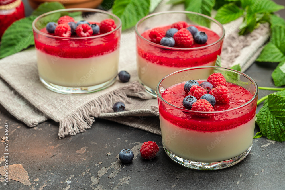 Delicious italian dessert panna cotta with berry sauce on a dark background in small jars. place for text - obrazy, fototapety, plakaty 