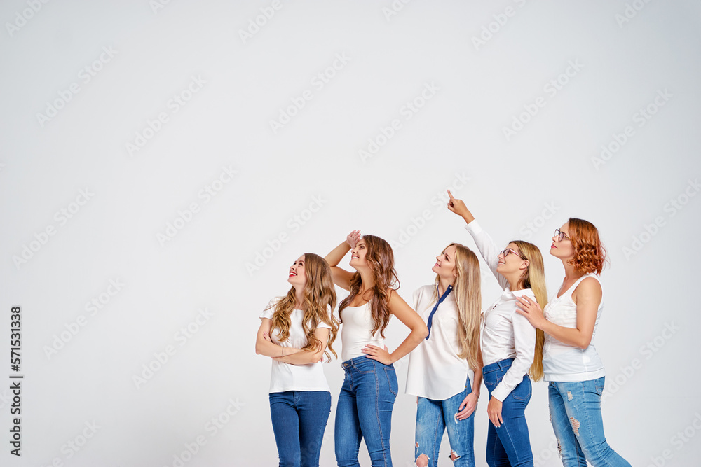 Naklejka premium Your tex here. Group of amazed young women looking up and pointing copy space on white background.