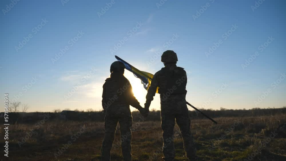Ukrainian army soldiers stands outdoor at sunset time and waves flag of ...