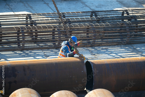 A slinger moves metal pipes at a construction site. Top view real workflow. Unloading materials for construction. photo