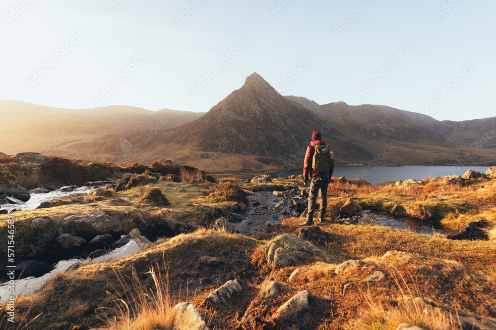 Person hiking in the mountains at sunrise next to a stream and lake
