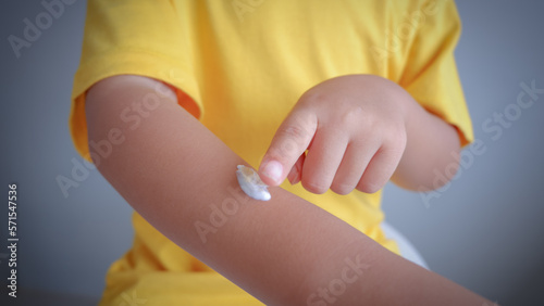 cute little asian girl wearing yellow t-shirt and applying cream on skin over grey