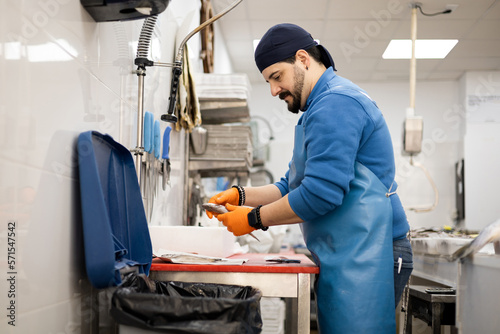 A uniformed middle-aged fishmonger is cleaning a small fish for a customer, selling food, a concept for small and medium-sized businesses.