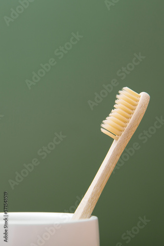 Wooden bamboo toothbrush in a white glass on a green background. The concept of sustainability and the rejection of plastic. The concept of hygiene and daily routine. Copy spase  vertical photo