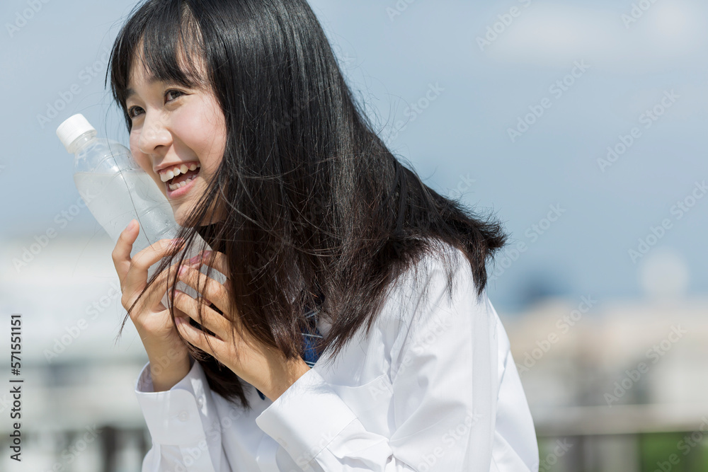 ペットボトルを頬にあてる女子学生