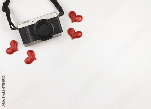 flat lay of digital camera with red glitter hearts on white background with copy space.