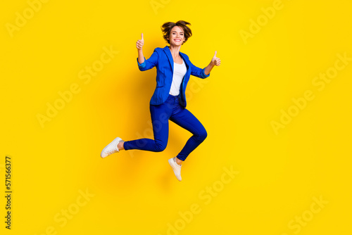 Full length photo of cute sweet lady dressed blue blazer jumping high showing two thumbs up isolated yellow color background