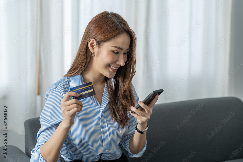 Cute and bright Asian businesswoman shopping online on mobile comfortably using a credit card to purchase goods for the convenience of spending at home on weekends. Cute and bright Asian businesswoman shopping online on mobile comfortably using a credit card to purchase goods for the convenience of spending at home on weekends.