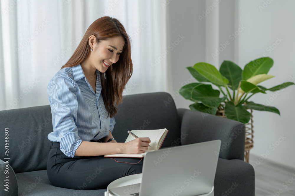 Confident Asian businesswoman sitting and taking notes in financial book Income tax with laptop computer or tablet in a happy office. Confident Asian businesswoman sitting and taking notes in financial book Income tax with laptop computer or tablet in a happy office.