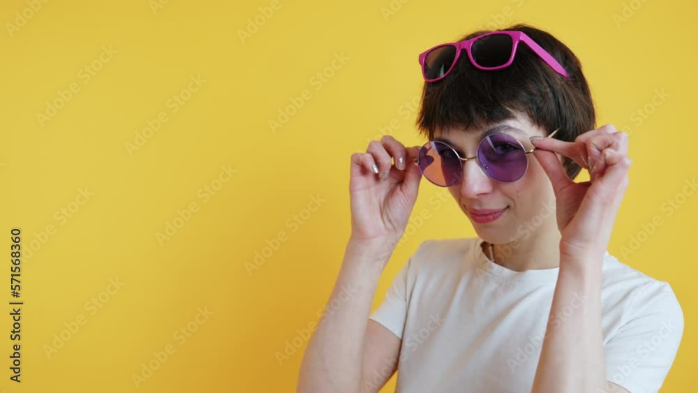 Young Short-Haired Woman Wearing Multiple Pairs of Sunglasses And Looking At Camera And Peaking Behind Glasses. Studio Shot. Orange Background. High quality 4k footage