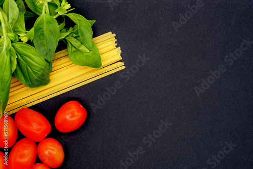 Dried pasta, basil and tomatoes on black background.