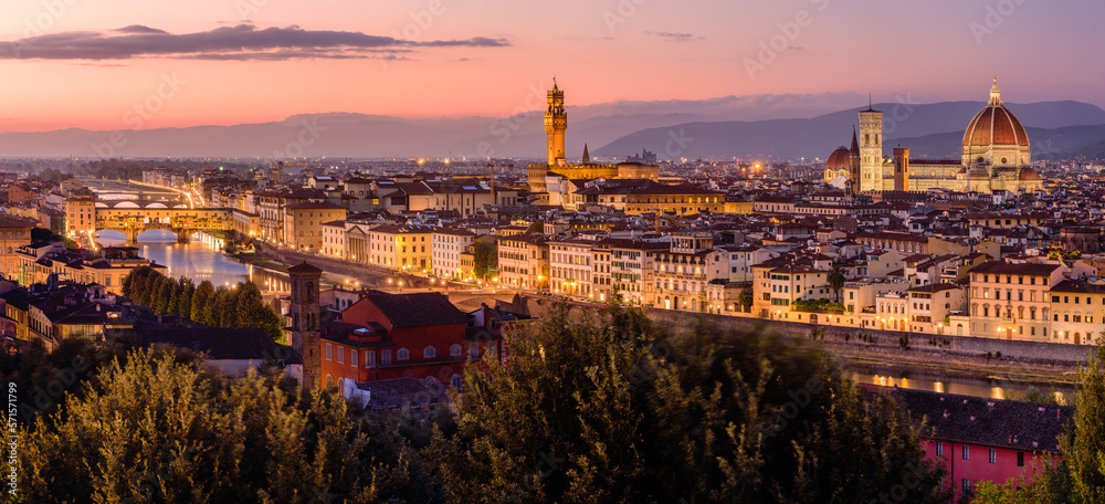 The illuminated Florence cityscape with the Ponte Vecchio over Arno river, the Palazzo Vecchio and the Florence Cathedral in an orange and purple twilight.