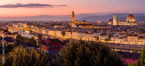 The illuminated Florence cityscape with the Ponte Vecchio over Arno river, the Palazzo Vecchio and the Florence Cathedral in an orange and purple twilight.