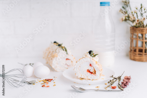 Meringue roll without sugar on a white plate cut into pieces in front of a bottle of milk and eggs.