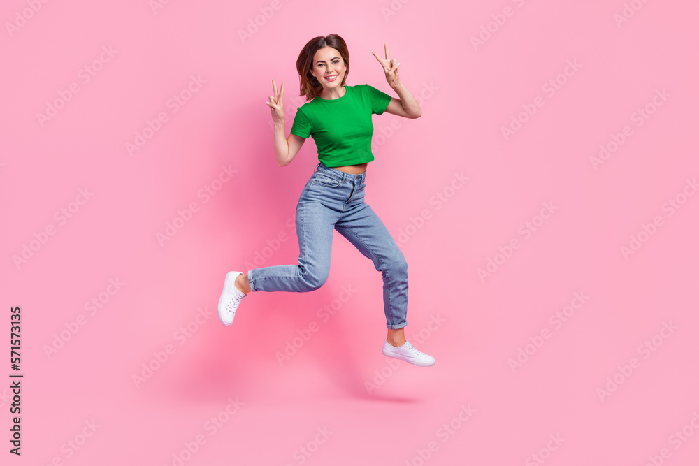 Full length photo of dreamy excited girl wear green crop showing v-signs jumping high isolated pink color background