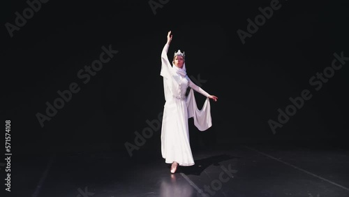The ballerina goes on stage. A ballet dancer in a beautiful white robe dances on a black background. Raymonda Variation. photo