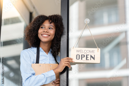 Foto African young woman starting a small business working in a cafe A coffee shop worker stands in front of the store opening an open sign and greets customers with happy smiles