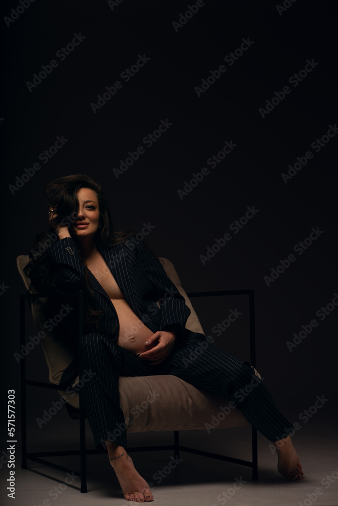 Beautiful pregnant girl at the studio. A pregnant girl in a man's suit.Stunning pregnant woman - maternity photography of a beautiful young expecting mother to be on a black background, studio photogr Beautiful pregnant girl at the studio. A pregnant girl in a man's suit.Stunning pregnant woman - maternity photography of a beautiful young expecting mother to be on a black background, studio photogr