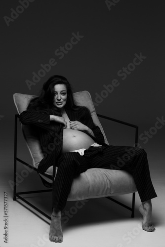 Beautiful pregnant girl at the studio. A pregnant girl in a man's suit.Stunning pregnant woman - maternity photography of a beautiful young expecting mother to be on a black background, studio photogr