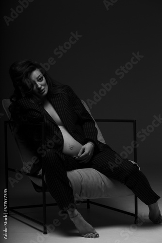 Beautiful pregnant girl at the studio. A pregnant girl in a man's suit.Stunning pregnant woman - maternity photography of a beautiful young expecting mother to be on a black background, studio photogr