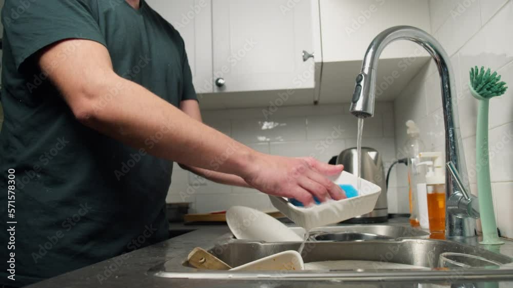 Male housewife washes a plate under running water in the sink in a modern kitchen. slow motion video of housewife using natural dishwashing detergent Male housewife washes a plate under running water in the sink in a modern kitchen. slow motion video of housewife using natural dishwashing detergent