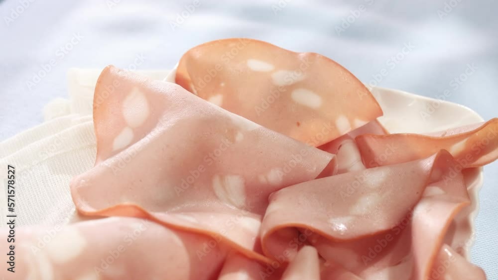 mortadella on a plate. Italian sausage on a table with a blue surface. serving meat delicacy. traditional boiled sausage under sunlight. mortadella on a plate. Italian sausage on a table with a blue surface. serving meat delicacy. traditional boiled sausage under sunlight.