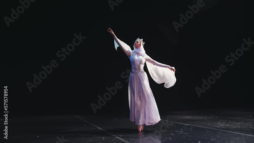 A ballerina in a beautiful white suit and a crown stands beautifully on the stage of the theater. The wind blows her clothes. The concept of freedom, determination. photo