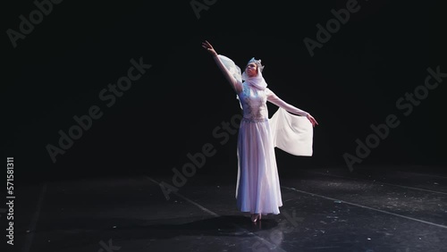 A ballerina in a beautiful white suit and a crown stands beautifully on the stage of the theater. The wind blows her clothes. The concept of freedom, determination. photo