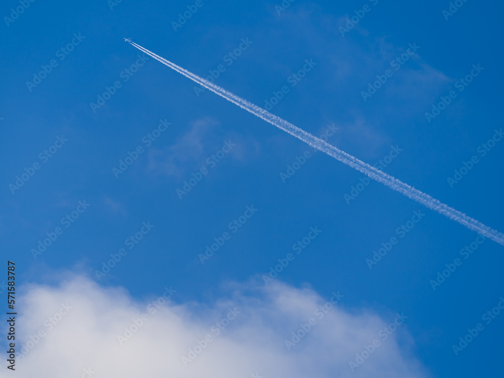 The plane leaves a white trail over white cloud in blue sky The plane leaves a white trail over white cloud in blue sky
