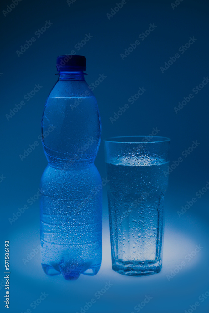 natural mineral healthy water in a transparent glass and drops of water splash out of the glass on a blue background. for signage banners labels postcards advertising