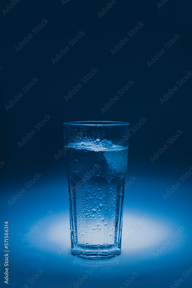 natural mineral healthy water in a transparent glass and drops of water splash out of the glass on a blue background. for signage banners labels postcards advertising natural mineral healthy water in a transparent glass and drops of water splash out of the glass on a blue background. for signage banners labels postcards advertising