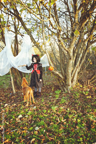 A girl in a carnival costume is training her puppy. A photo with elements of the Halloween holiday, where the child and the puppy. © lexashka