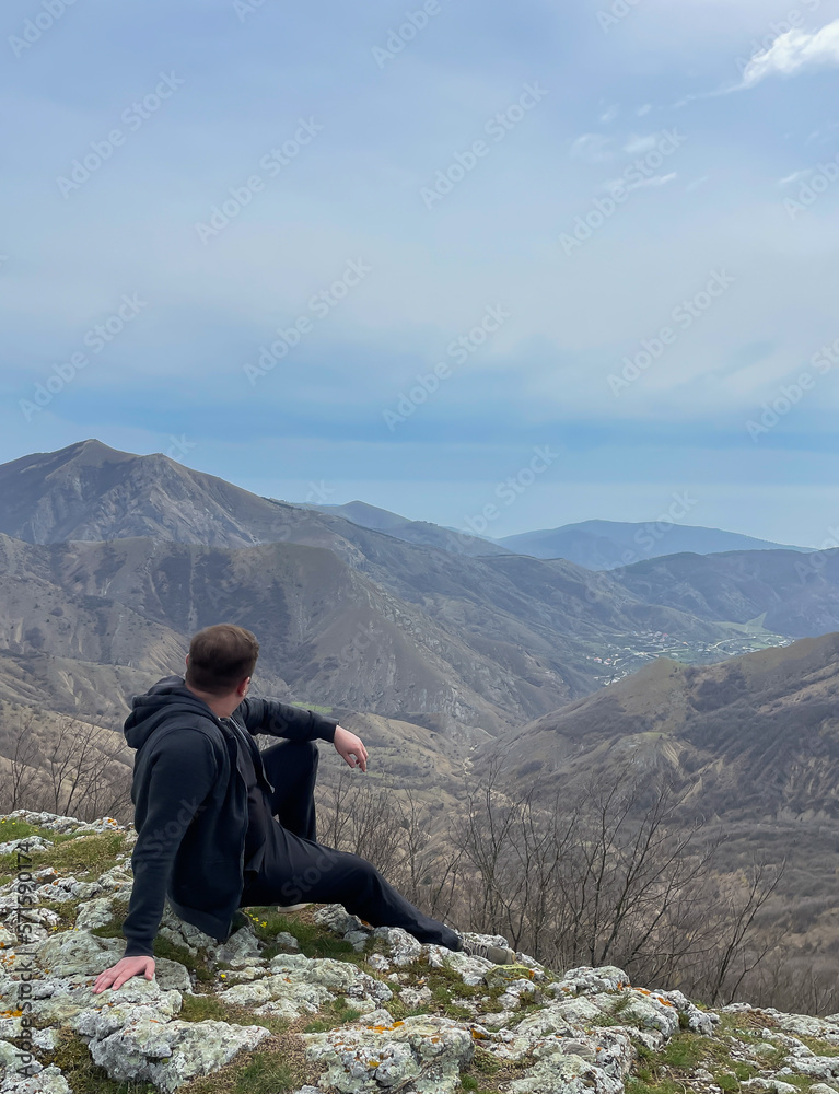 A man sits on a mountain and looks into the distance nature hiking on foot travel A man sits on a mountain and looks into the distance nature hiking on foot travel