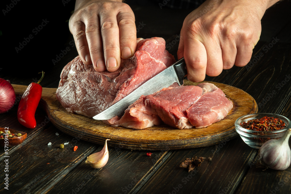 Hands cook cut raw meat with a knife before grilling. Preparing beef meat before roasting. Working environment in the kitchen of a restaurant or hotel