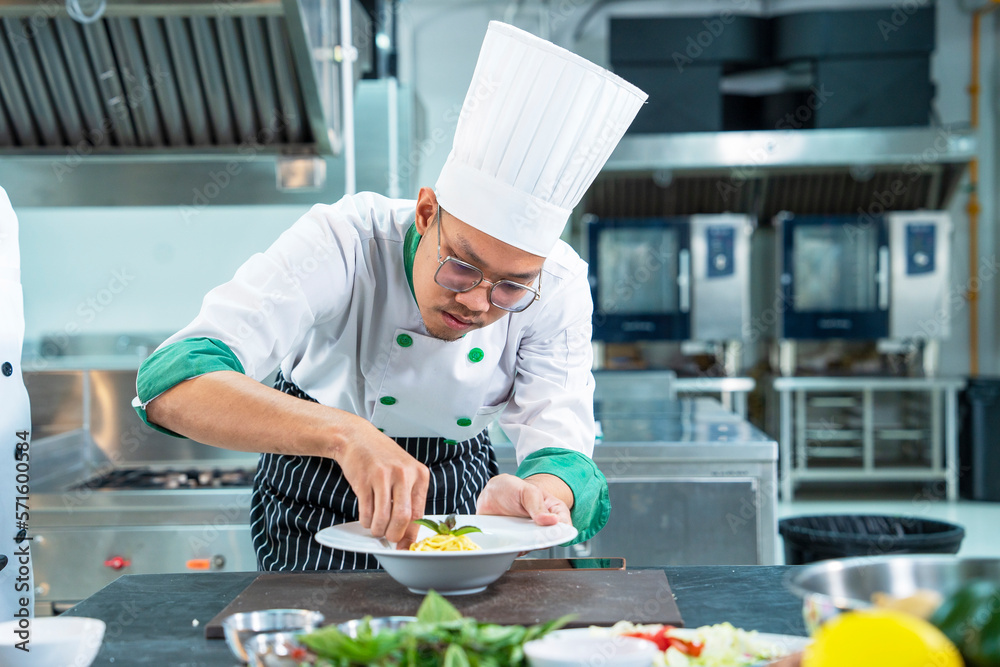 Asian male chefs wearing uniforms laying plates of spaghetti and vegetables for lunch in a restaurant
