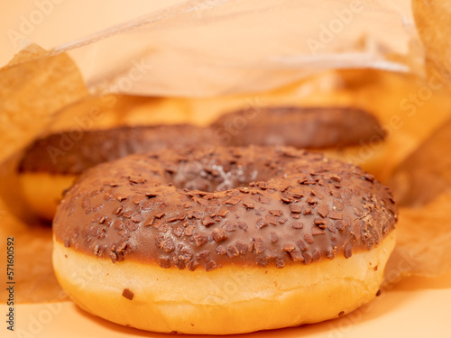 Chocolate donut with chocolate chips in a paper bag on an orange background. close-up.