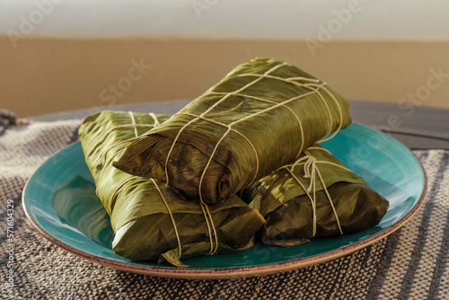 Hallaca or Tamale wrapped with plantain leaves over a rustic table and a blue dish, Mexican and Venezuelan traditional food for Christmas  made or corn dough photo