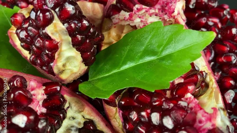 Close-up rotating open pomegranate pieces with ruby arils green leaf studio light. Juicy seed pods tropical fruit indoors. Rotation sweet ready to eat vegetarian food. Organic antioxidant. Merchandise