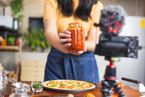 Young attractive Asian woman talking communicating during online live streaming how to cook homemade pizza indoor kitchen. content creator using camera recording food product review.