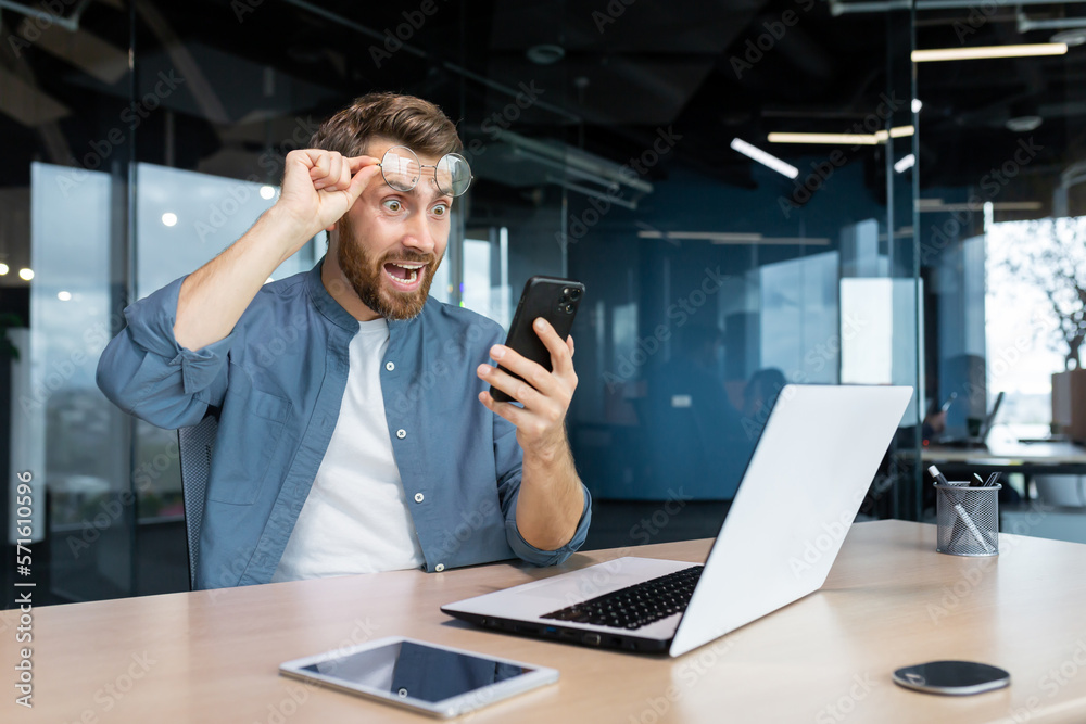 Φωτογραφία Mature man shocked by bad news and online notification received on phone, businessman at work frustrated and shouting at smartphone screen, worker at workplace sitting with laptop
